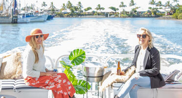 two young women sitting, laughing and enjoying a drink on a moving boat.